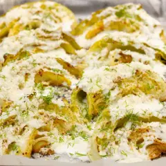 Pieczona kapusta z piekarnika, polana sosem i posypana serem i koperkiem.