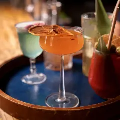 Kolorowe drinki na tacy. Pomarańczowy koktajl z suszoną pomarańczą, zielony drink i czerwony z oliwkami. Idealne na wieczór, by dowiedzieć się, jak pić metaxę.