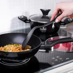 Dłoń miesza makaron w woku na płycie indukcyjnej. W tle garnek. To pokazuje, jak się mierzy średnicę patelni.