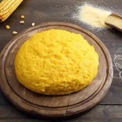 Puszysta polenta z mąki kukurydzianej na drewnianej desce, obok kolby kukurydzy i garści mąki.