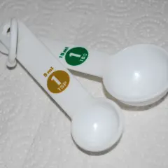 Dwie białe łyżki miarowe. Jedna ma oznaczenie 5 ml (1 TSP), druga 15 ml (1 TBS).
