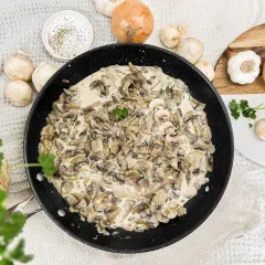 Kremowy sos pieczarkowy w patelni, gotowy do podania. Obok składniki: pieczarki, cebula, czosnek, przyprawy. Idealny sos pieczarkowy przepis.