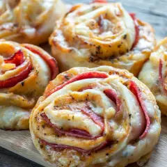 Pyszne przekąski z ciasta na pizzę z serem i wędliną, ułożone na desce.