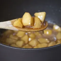 Kawałki jabłek gotujące się w syropie na łyżce, idealne, by pokazać, jak zagęścić jabłka do szarlotki budyniem.
