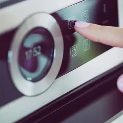 Dłoń naciska ikonę termoobiegu na panelu piekarnika Amica.