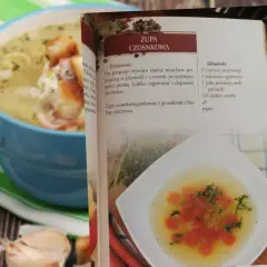Zupa czosnkowa w niebieskiej misce, obok otwarta książka kucharska z przepisem.