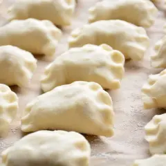 Surowe ciasto na pierogi z olejem, uformowane w kształt półksiężyców, leży na blacie posypanym mąką.