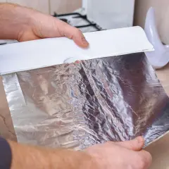 Ręce trzymają folię aluminiową z dozownika. Czy można użyć folii aluminiowej zamiast papieru do pieczenia? Tak, to świetna alternatywa!