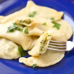 Pyszne pierogi z farszem ze szpinaku, udekorowane natką pietruszki, prezentowane na niebieskim talerzu. Widoczny widelec pokazuje bogate wnętrze.