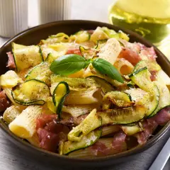 Makaron z cukinią i szynką parmeńską, ozdobiony bazylią. Idealne szybkie dania z cukinią na obiad.