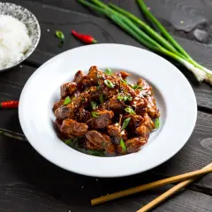 Pyszny kurczak po wietnamsku na gorącym półmisku, posypany szczypiorkiem i sezamem, obok miseczka ryżu i papryczki chili.