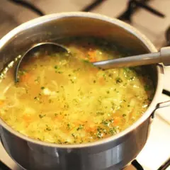 Gorący rosół w garnku, z widoczną chochlą. Kiedy dodać kostkę rosołową do rosołu? Najlepiej pod koniec gotowania, by wzmocnić smak.