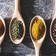 Cztery drewniane łyżki wypełnione przyprawami: papryką, zielonym pieprzem, curry i czarnym pieprzem. Ile łyżeczek ma łyżka?