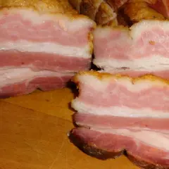 Kawałki wędzonego boczku na desce, obok czosnek i pomidor. Idealne do tego, jak sparzyć boczek wędzony.