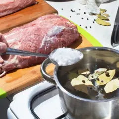 Ręka wsypuje sól do garnka z wodą, liśćmi laurowymi i pieprzem. Przygotowanie solanki: ile łyżek soli na litr wody?