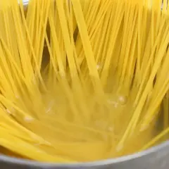 Długie, żółte nitki makaronu spaghetti gotują się w bulgoczącej wodzie. Kluczowe jest, ile posolić makaron, by był idealny.
