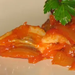 Śledzie po żydowsku w sosie pomidorowym z cebulą, ozdobione natką pietruszki. Pyszny przepis na śledzie.