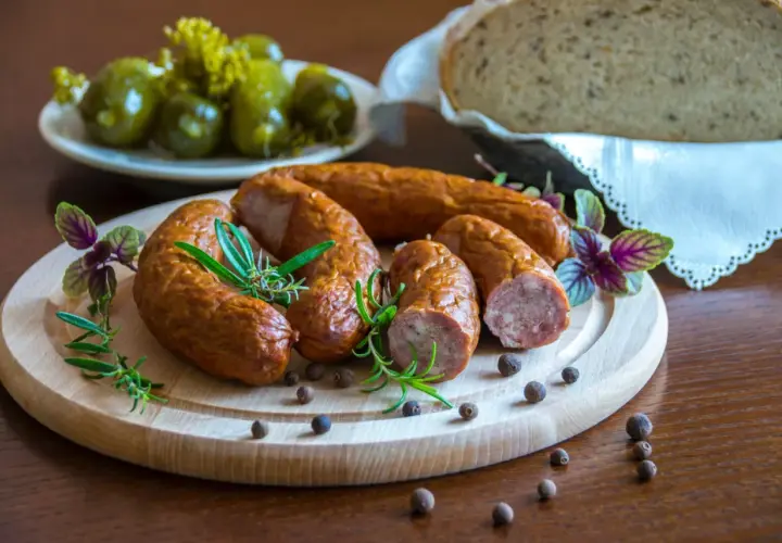 Swojska kiełbasa na desce z rozmarynem i pieprzem. Obok ogórki i chleb. Idealna ilość soli do kiełbasy swojskiej.