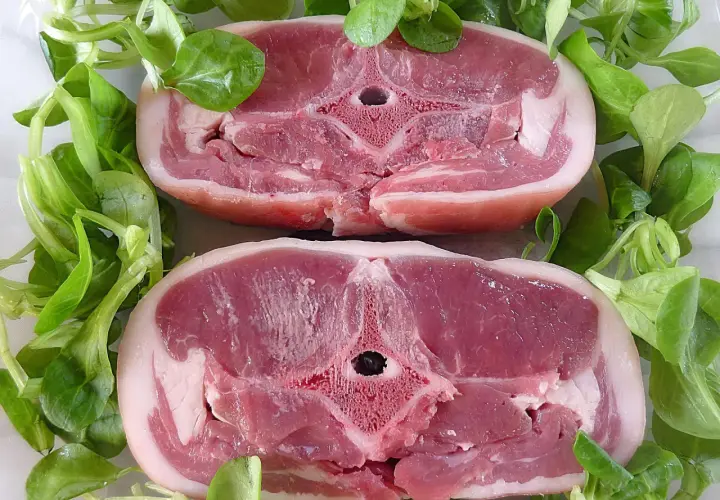 Dwa soczyste kotlety jagnięce otoczone świeżą sałatą. Zastanawiasz się, ile kosztuje kilogram jagnięciny?