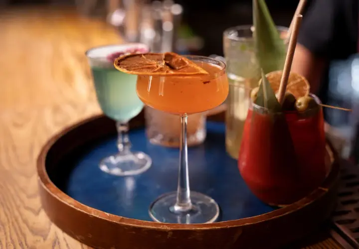 Kolorowe drinki na tacy. Pomarańczowy koktajl z suszoną pomarańczą, zielony drink i czerwony z oliwkami. Idealne na wieczór, by dowiedzieć się, jak pić metaxę.