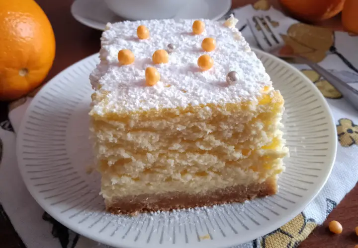 Sernik z puszystym nadzieniem na kruchym spodzie z herbatników i masła, posypany cukrem pudrem i pomarańczowymi perełkami.