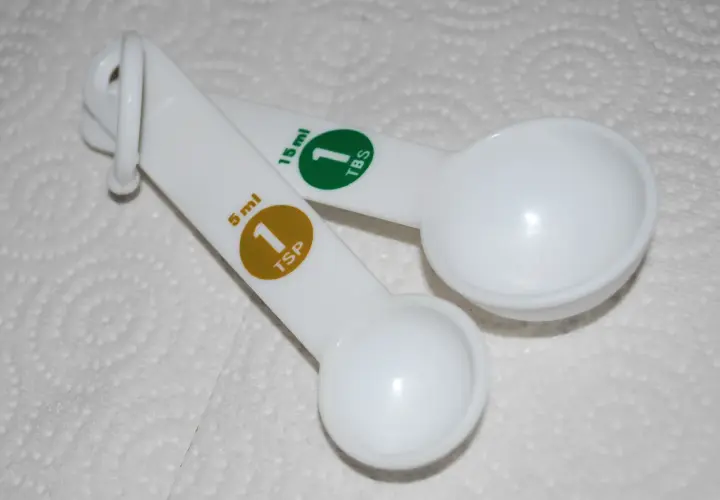Dwie białe łyżki miarowe. Jedna ma oznaczenie 5 ml (1 TSP), druga 15 ml (1 TBS).