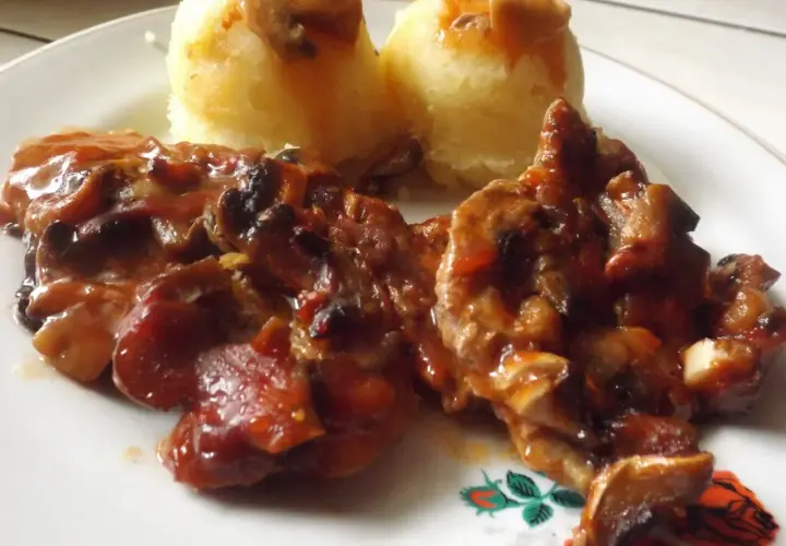 Karkówka z pieczarkami i cebulą w sosie, podana z puree ziemniaczanym. Danie polane ketchupem.
