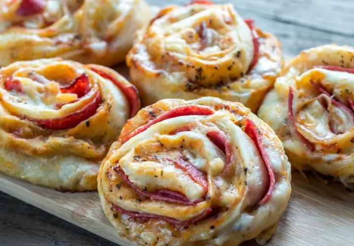 Pyszne przekąski z ciasta na pizzę z serem i wędliną, ułożone na desce.