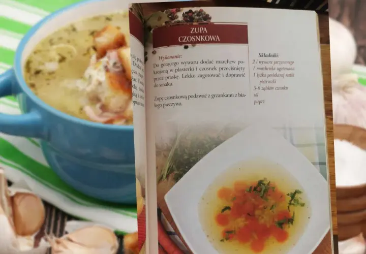Zupa czosnkowa w niebieskiej misce, obok otwarta książka kucharska z przepisem.
