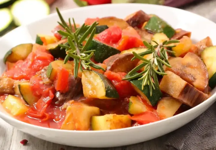 Pyszny bigos z cukinii wegetariański, duszony z pomidorami i ziołami, podany w białej misce.
