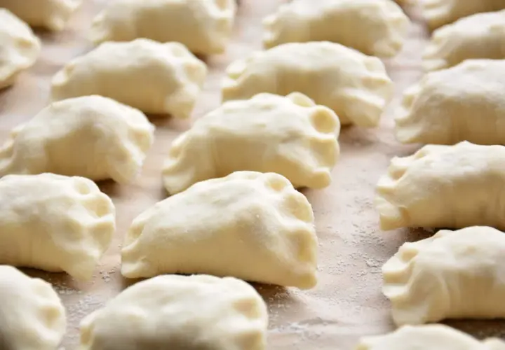 Surowe ciasto na pierogi z olejem, uformowane w kształt półksiężyców, leży na blacie posypanym mąką.