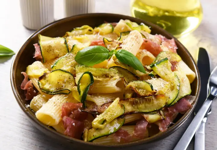 Makaron z cukinią i szynką parmeńską, ozdobiony bazylią. Idealne szybkie dania z cukinią na obiad.