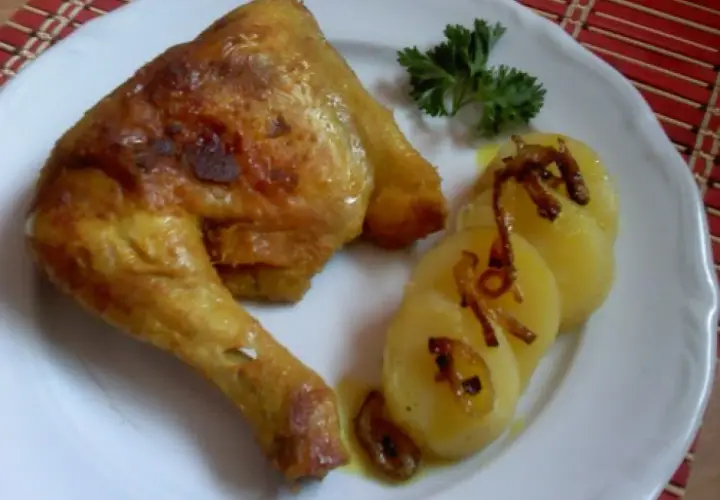 Pieczone udka kurczaka z ziemniakami i natką pietruszki na białym talerzu.