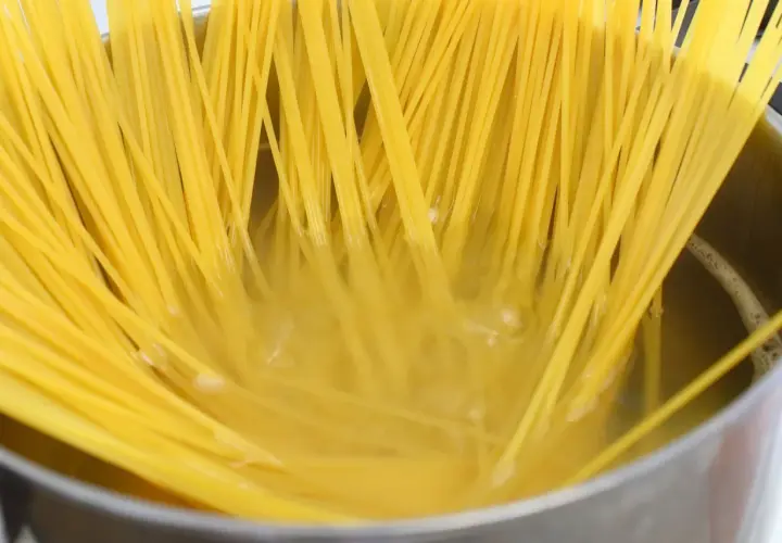 Długie, żółte nitki makaronu spaghetti gotują się w bulgoczącej wodzie. Kluczowe jest, ile posolić makaron, by był idealny.