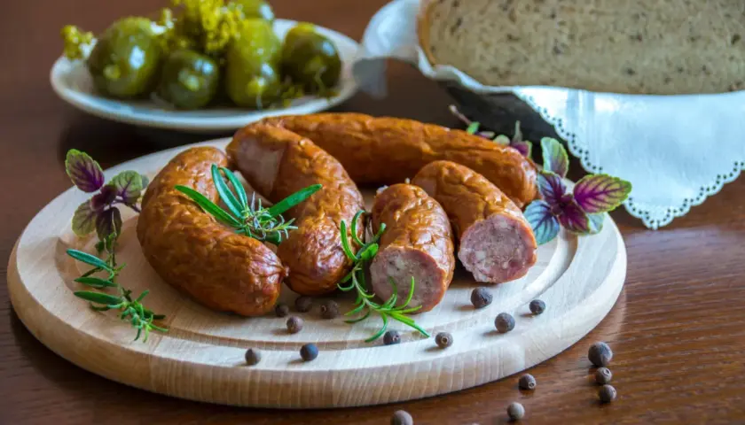 Swojska kiełbasa na desce z rozmarynem i pieprzem. Obok ogórki i chleb. Idealna ilość soli do kiełbasy swojskiej.