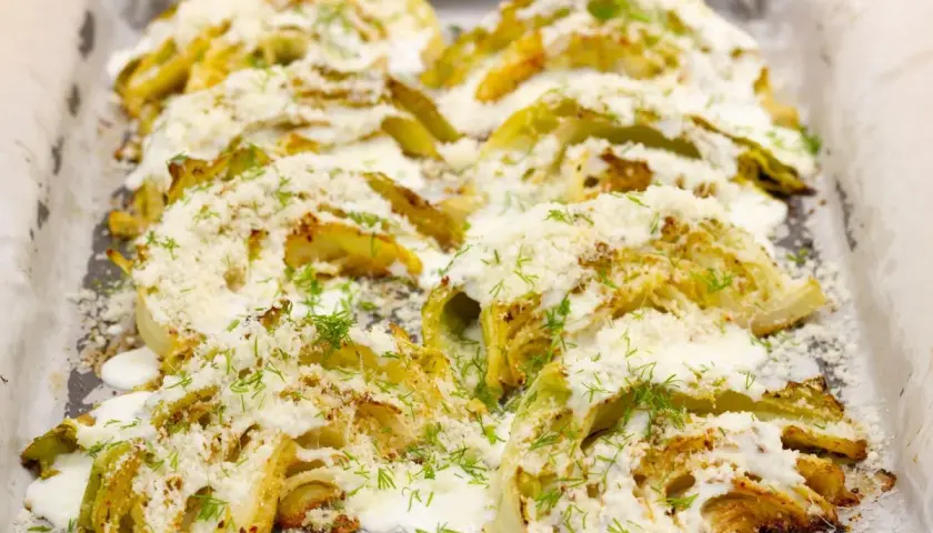 Pieczona kapusta z piekarnika, polana sosem i posypana serem i koperkiem.