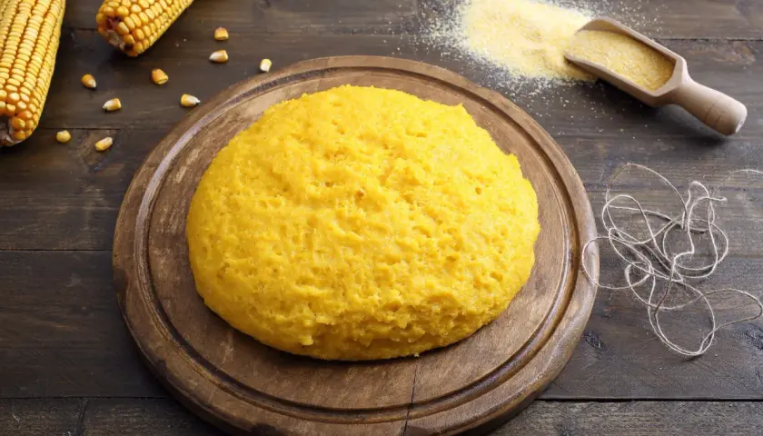 Puszysta polenta z mąki kukurydzianej na drewnianej desce, obok kolby kukurydzy i garści mąki.