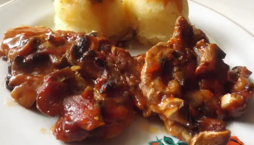Karkówka z pieczarkami i cebulą w sosie, podana z puree ziemniaczanym. Danie polane ketchupem.