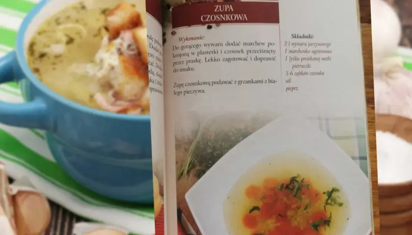 Zupa czosnkowa w niebieskiej misce, obok otwarta książka kucharska z przepisem.