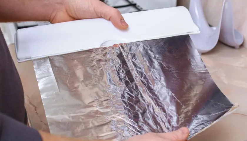 Ręce trzymają folię aluminiową z dozownika. Czy można użyć folii aluminiowej zamiast papieru do pieczenia? Tak, to świetna alternatywa!
