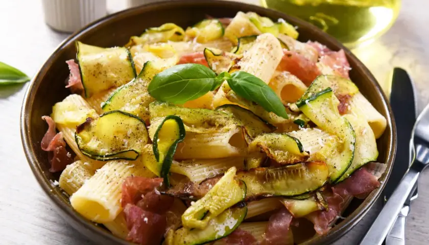 Makaron z cukinią i szynką parmeńską, ozdobiony bazylią. Idealne szybkie dania z cukinią na obiad.