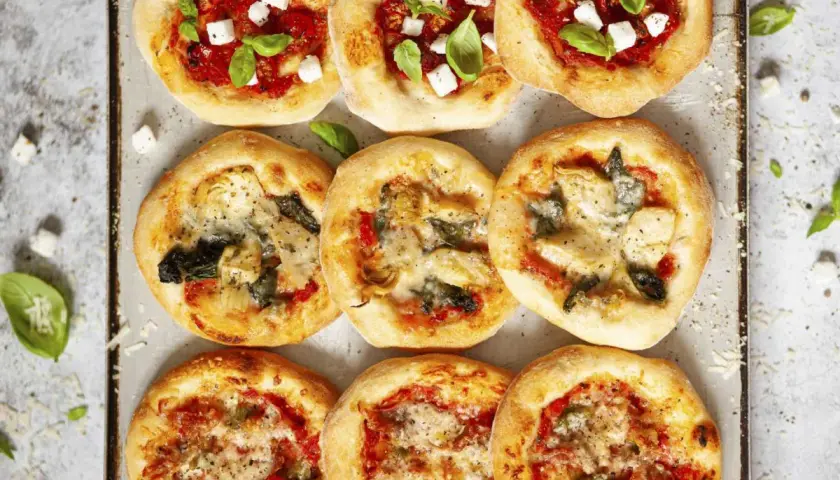 Mini pizze z ciasta na pizzę, niektóre z serem i bazylią, inne z warzywami.