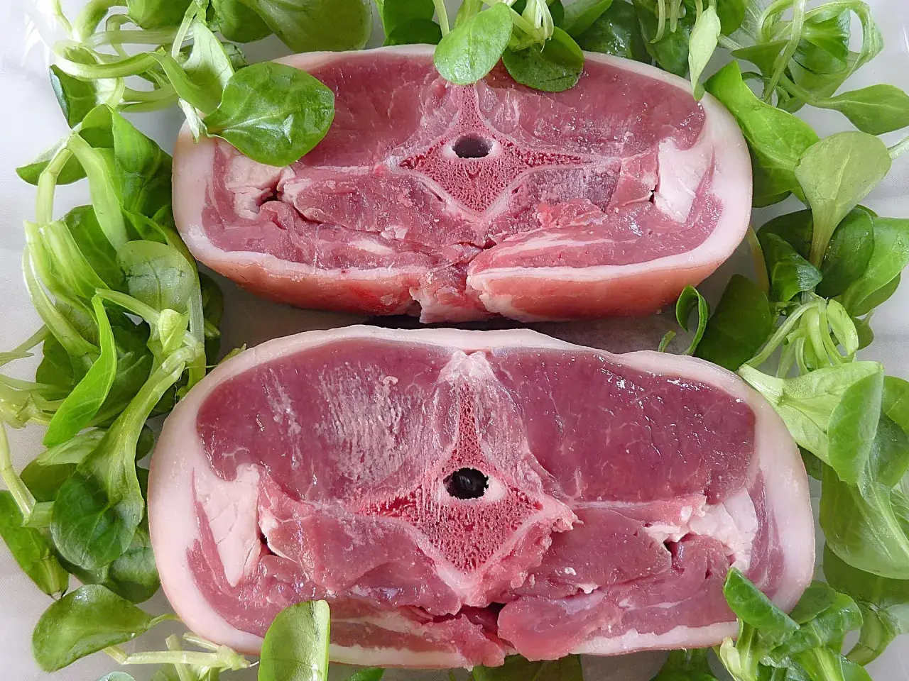 Dwa soczyste kotlety jagnięce otoczone świeżą sałatą. Zastanawiasz się, ile kosztuje kilogram jagnięciny?