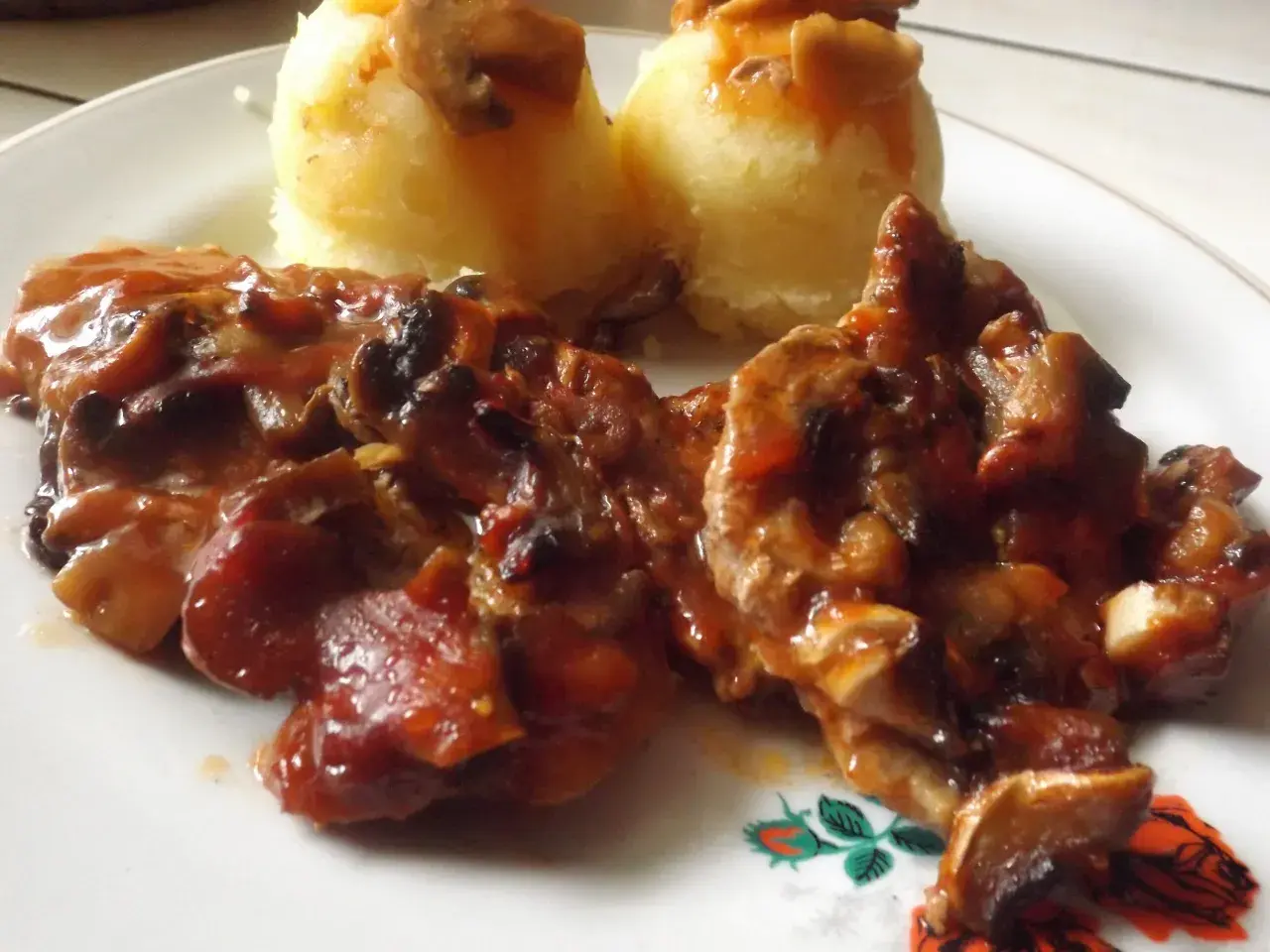 Karkówka z pieczarkami i cebulą w sosie, podana z puree ziemniaczanym. Danie polane ketchupem.