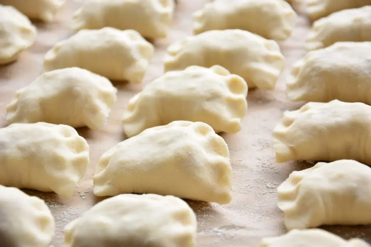 Surowe ciasto na pierogi z olejem, uformowane w kształt półksiężyców, leży na blacie posypanym mąką.
