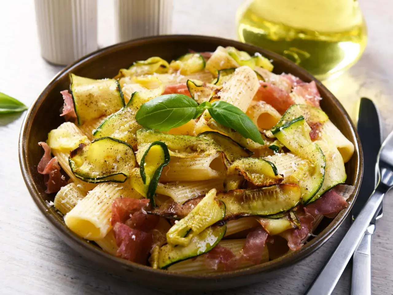 Makaron z cukinią i szynką parmeńską, ozdobiony bazylią. Idealne szybkie dania z cukinią na obiad.