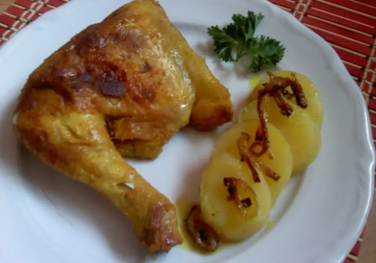 Pieczone udka kurczaka z ziemniakami i natką pietruszki na białym talerzu.