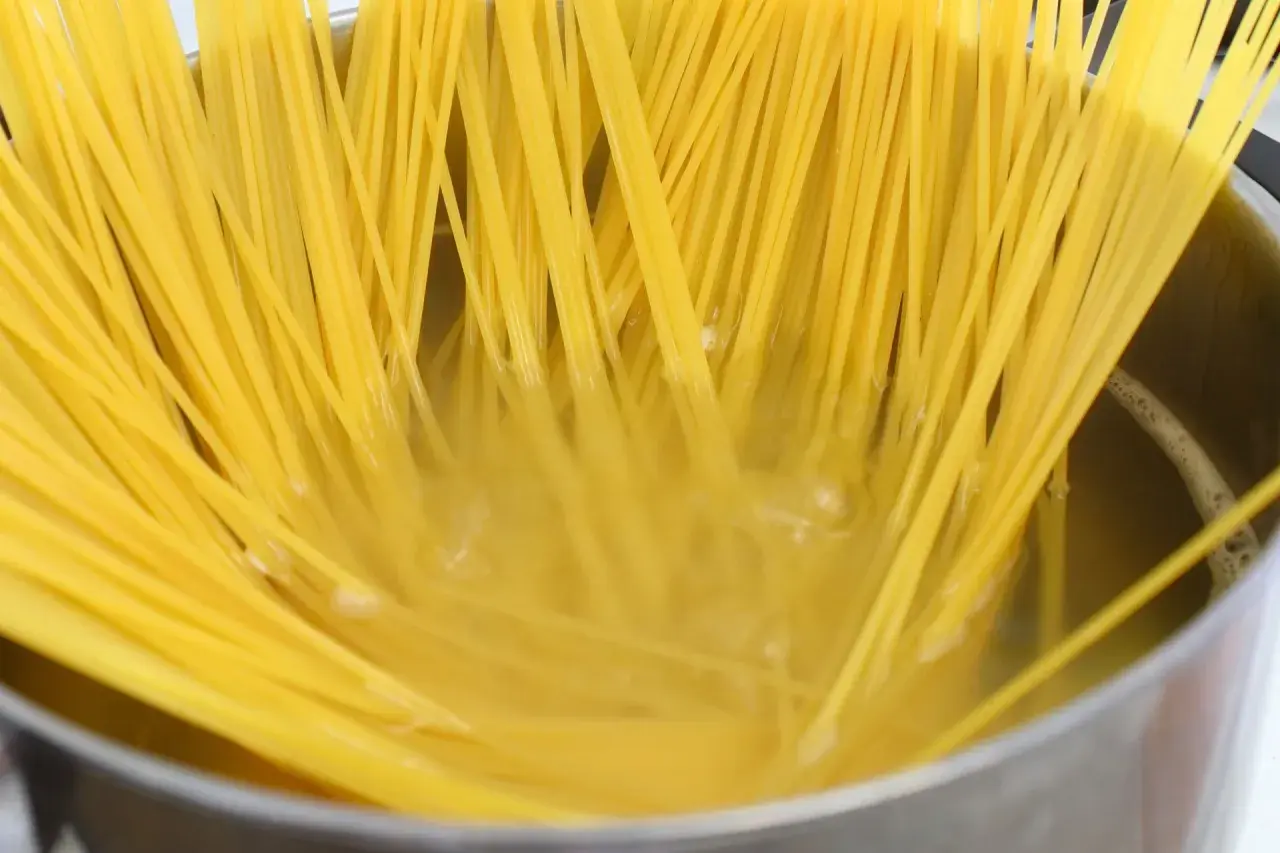 Długie, żółte nitki makaronu spaghetti gotują się w bulgoczącej wodzie. Kluczowe jest, ile posolić makaron, by był idealny.