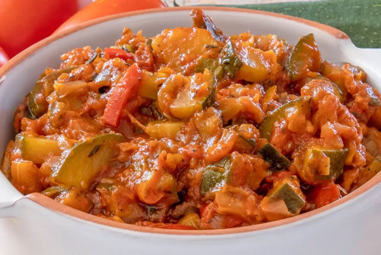 Pyszny, wegetariański bigos z cukinii z pomidorami i papryką, podany w białej misce.