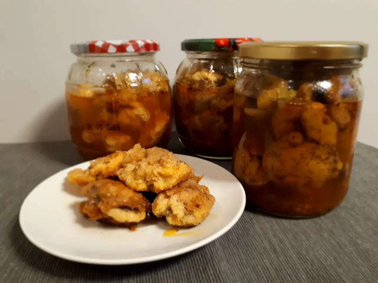 Słoiki z marynowanymi pieczarkami, obok talerzyk z kilkoma pieczarkami w panierce. Idealne na pieczarki marynowane przepis.